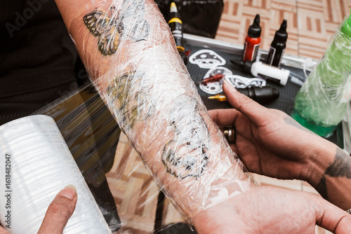 Tableau sur toile Tattoo artist covers newly finished forearm tattoos with transparent plastic wrap to protect skin and preserve ink during healing