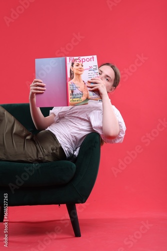 Woman with lifestyle magazine on armchair against red background