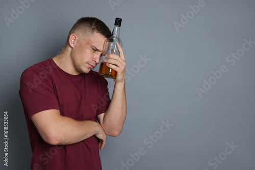 Foto Man with bottle of whiskey suffering from hangover on grey background, space for