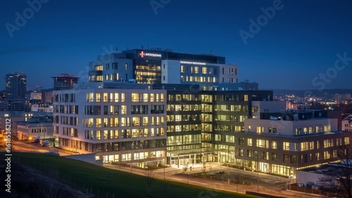 Modern hospital building illuminated at night with large glass windows and surrounding cityscape