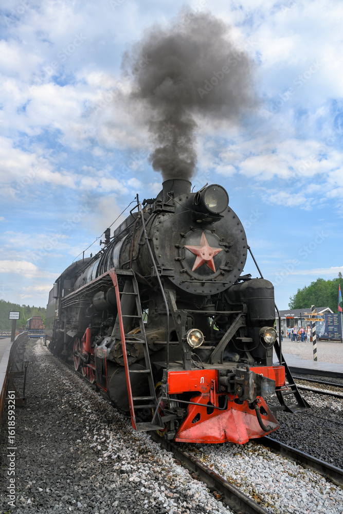 Fototapeta premium A retro steam locomotive of the mid-20th century with a smoking pipe arrives at the Ruskeala station in Karelia