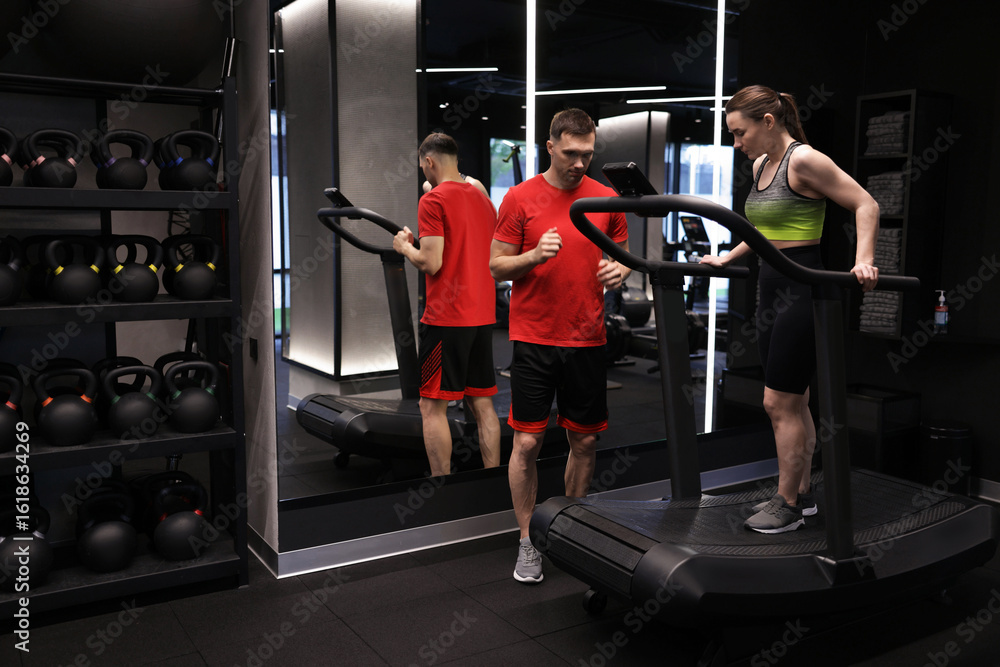 Fototapeta premium Young woman exercising on treadmill with professional personal trainer in gym