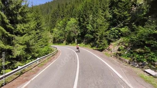 Cyclist rides along a scenic mountain road surrounded by lush green forest. Perfect for travel, sports, and nature themes. High-quality photo showcasing active lifestyle and breathtaking scenery.