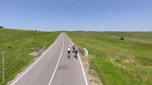 Four cyclists ride along a scenic country road on a sunny day.  Perfect for travel, sports, and active lifestyle imagery.  High-quality drone footage.