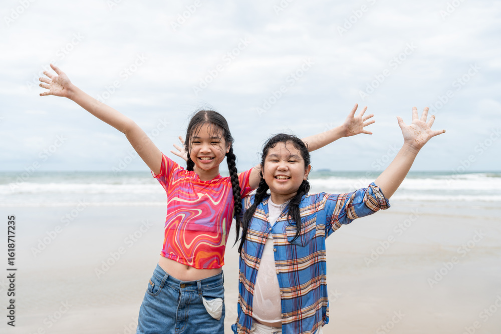 Two young girls joyfully smiling and raising their arms on the beach after playing in the sea. Asian children on cheerful vacation in summer. Two young girls joyfully smiling and raising their arms on the beach after playing in the sea. Asian children on cheerful vacation in summer.