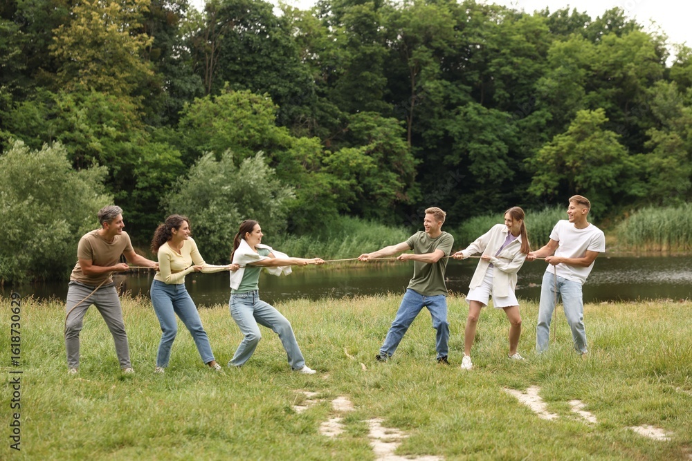 Obraz premium Team building. Group of happy people playing tug of war with rope outdoors