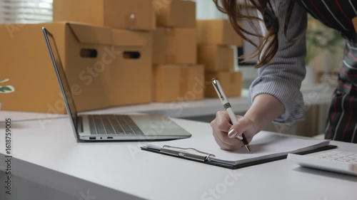 Woman working from home office, using laptop for online marketing, preparing product packages for customer delivery while managing small business startup operations