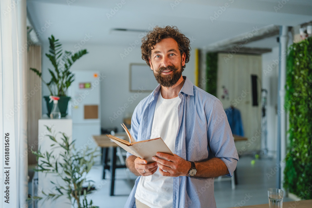 Fototapeta premium Smiling freelancer reading a book in sustainable home office