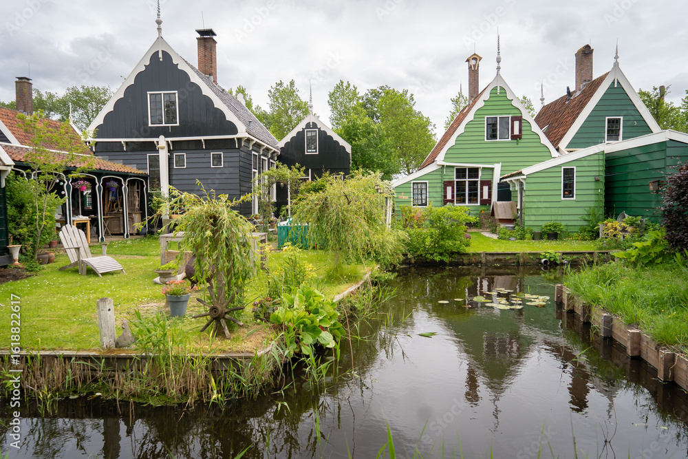 Obraz premium Dutch typical landscape. Traditional old dutch windmill with old houses against blue cloudy sky in the Zaanse Schans village, Netherlands. Famous tourism place. Sheep grazing on green grass.