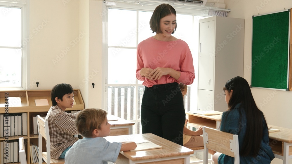 Caucasian teacher walking and check student homework at classroom while diverse children doing classwork at classroom. Diverse smart student lecturing and taking a note at elementary school. Pedagogy. Caucasian teacher walking and check student homework at classroom while diverse children doing classwork at classroom. Diverse smart student lecturing and taking a note at elementary school. Pedagogy.
