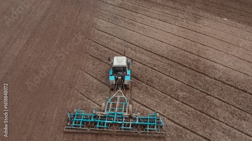 A tractor with a grain seeder is working in the field. Birds are flying around.