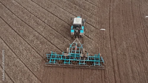 Top down view of a tractor with a grain seeder is working in the field