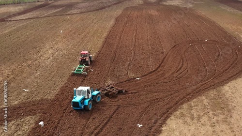 Two tractors with a grain seeders is working in the field. Shooted by drone