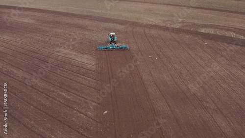 Aerial view of the tractor with a grain seeder is working in the field. Birds are flying around