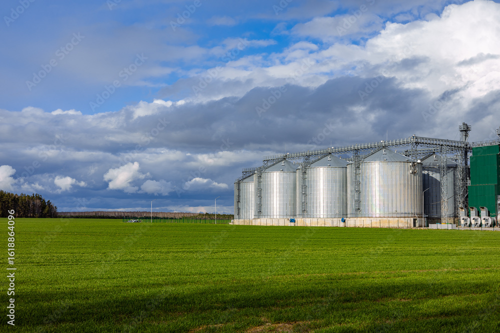 Steel grain storage silos with a conical base can be used for various purposes. Industrial facilities of feeding and flour mills. Against the backdrop of a beautiful sky with clouds. Steel grain storage silos with a conical base can be used for various purposes. Industrial facilities of feeding and flour mills. Against the backdrop of a beautiful sky with clouds.
