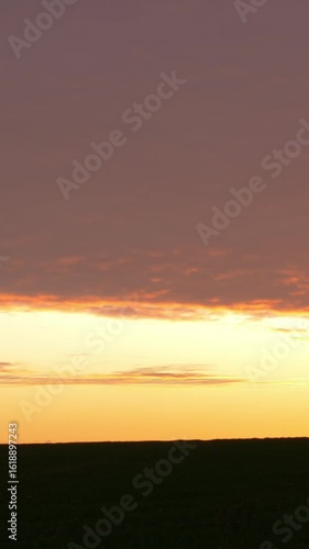 Vertical video of sunset sky above field with golden hues, capturing the warm and serene evening landscape