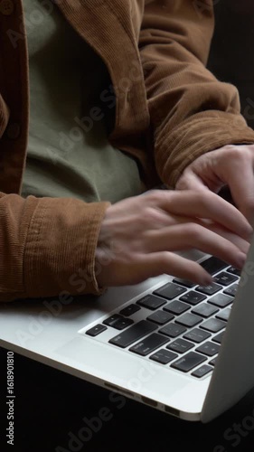 Vertical video of close-up female hands typing on laptop keyboard with light streaming through window