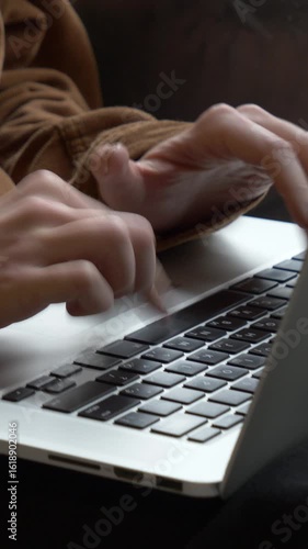 Vertical video of close-up female hands typing on laptop keyboard with light streaming through window