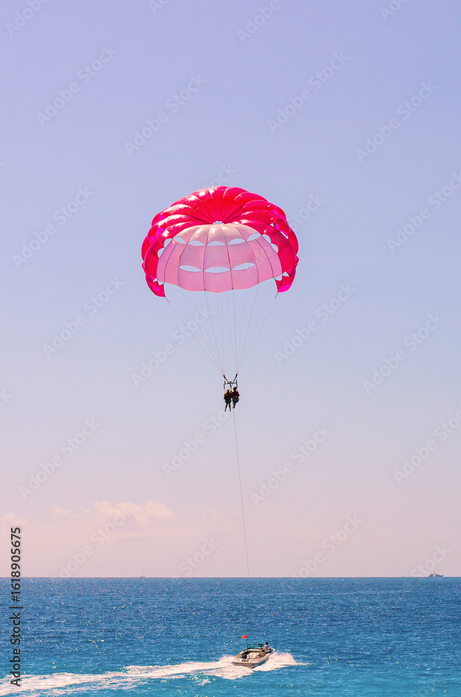 Motorboat towing two parachutists above calm sea under bright blue sky Motorboat towing two parachutists above calm sea under bright blue sky
