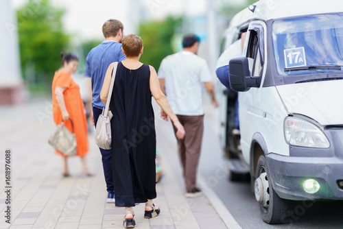 People boarding a minibus on a busy street in an urban area during a sunny day
