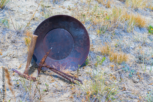 Obraz na plátne Gold-pan & mining picks rest in desert  showing landscape soil, mountain background