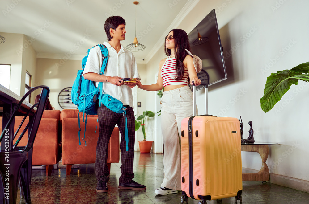 Fototapeta premium Young latin american couple arriving at hotel lobby handing over passport and credit card to receptionist for check in