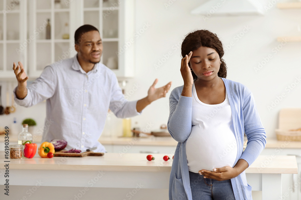 Obraz premium African american guy shouting at his pregnant wife, kitchen interior. Upset black expecting lady having headache while her furious husband yelling at her, family having fight while cooking together