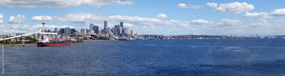 Seattle skyline panorama revealing Lumen Field, industrial cranes, Puget Sound beneath vibrant blue sky with wispy cloud formations Seattle skyline panorama revealing Lumen Field, industrial cranes, Puget Sound beneath vibrant blue sky with wispy cloud formations
