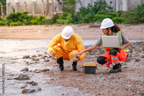 Foto Two environmental engineers in safety gear work at a shoreline near gas storage tanks