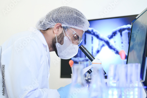 Bild auf Leinwand A geneticist in full PPE intently analyzes a sample through a microscope in a modern lab