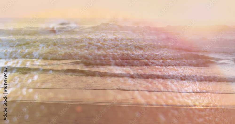 Obraz premium Rolling gentle ocean waves reflecting pastel sky at sunset on sandy shore, with sun glare