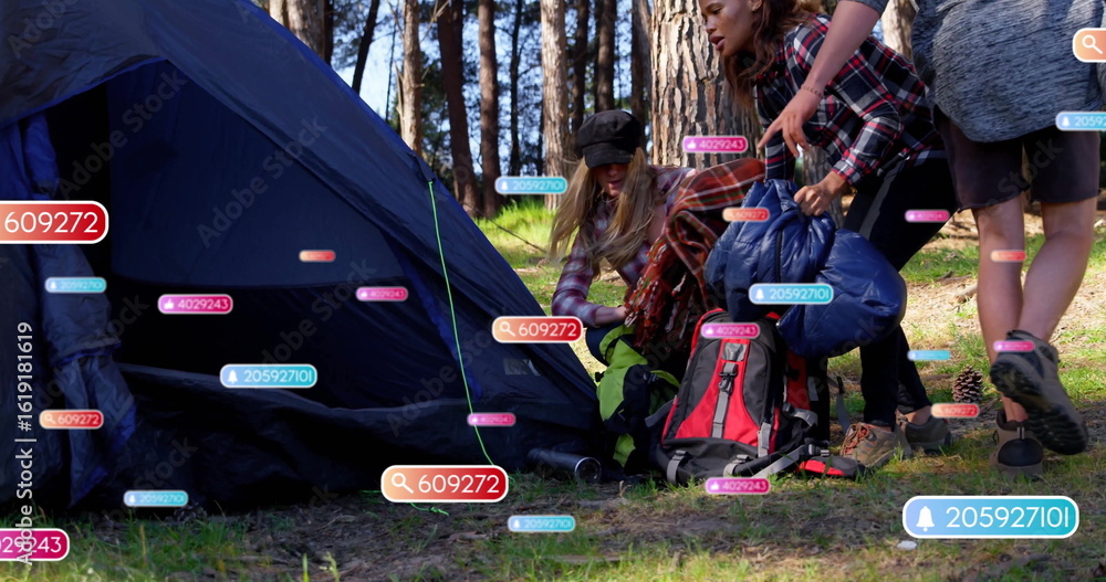 Fototapeta premium Assembling campers in hiking gear raising blue tent in forest clearing with AR labels, copy space
