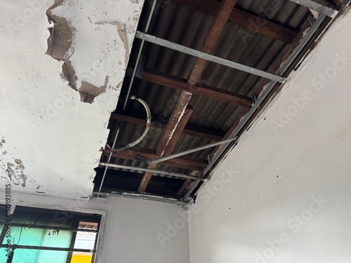 A collapsed section of a house roof reveals a gaping hole caused by a fire, with visible burn marks and fallen ceiling material exposing internal metal structures. 