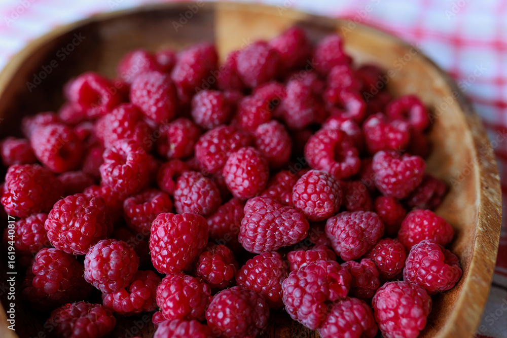 A wooden bowl with ripe raspberries lies on a rustic tablecloth. A wooden bowl with ripe raspberries lies on a rustic tablecloth.