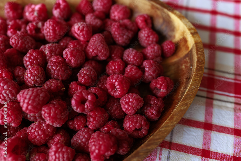 A wooden bowl with ripe raspberries lies on a rustic tablecloth. A wooden bowl with ripe raspberries lies on a rustic tablecloth.