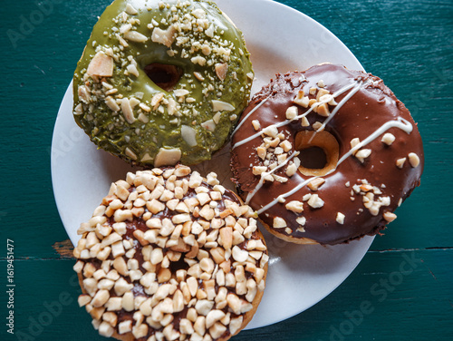 Photography 3 donuts on a plate, chocolate peanut and green tea donuts on the table, green background, top view