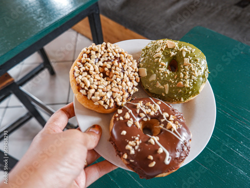 3 Donuts with varios flavour, chocolate, peanut and green tea donuts on the table, green background, top view, served by white plate, held by hand