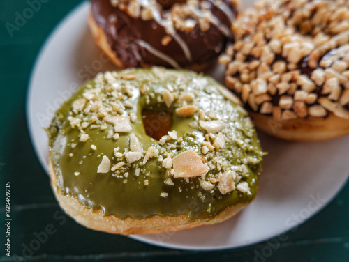 close up picture of donuts with various flavour. matcha, peanut and chocolate donuts in white plate