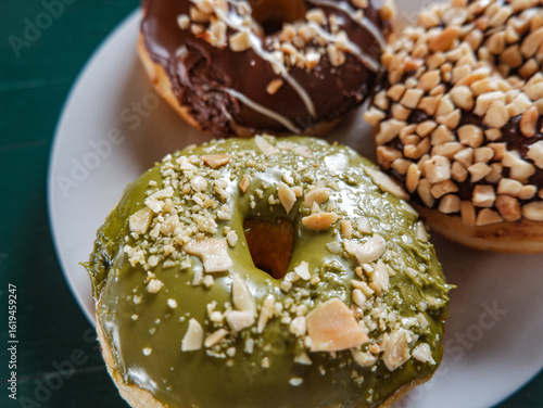 close up picture of donuts with various flavour. matcha, peanut and chocolate donuts in white plate