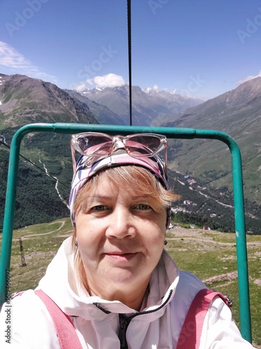 A selfie of a female tourist on a cable car in front of mountain peaks, close-up.
