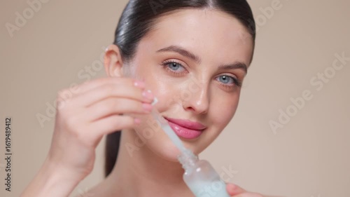 Young beautiful woman applying face serum with pipette on her face close up. Cosmetic procedures for facial skin care