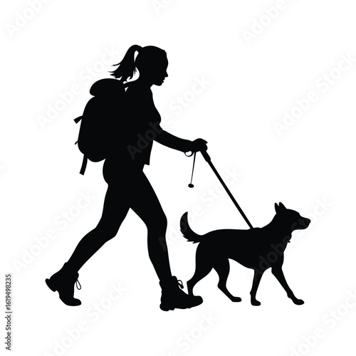 Silhouette of a woman hiking with her dog using trekking poles outdoors