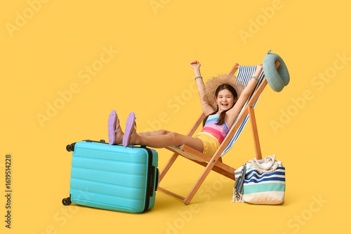 Foto Cute girl with suitcase and neck pillow sitting in deck chair on yellow backgrou