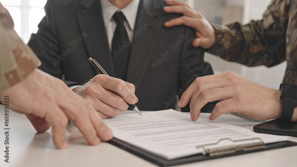 Fototapeta premium A man signs a document as others offer support. The scene is focused, highlighting collaboration and agreement.