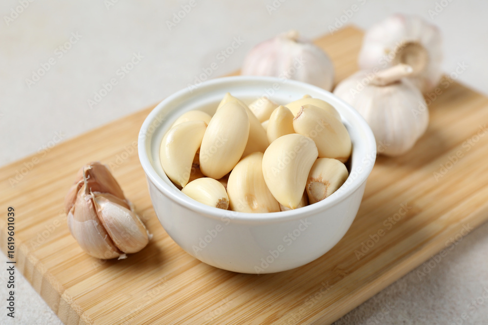 Wooden board with fresh garlics and bowl of cloves on white background, closeup Wooden board with fresh garlics and bowl of cloves on white background, closeup