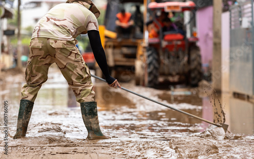 Thai workers cleaning a mud-covered street after a major flood. Wearing safety gear, they work together to restore public roads, showing resilience and community effort in disaster recovery