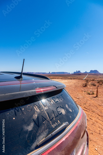 A dirty car displaying the word valley prominently on its back window with Monument Valley in background, USA