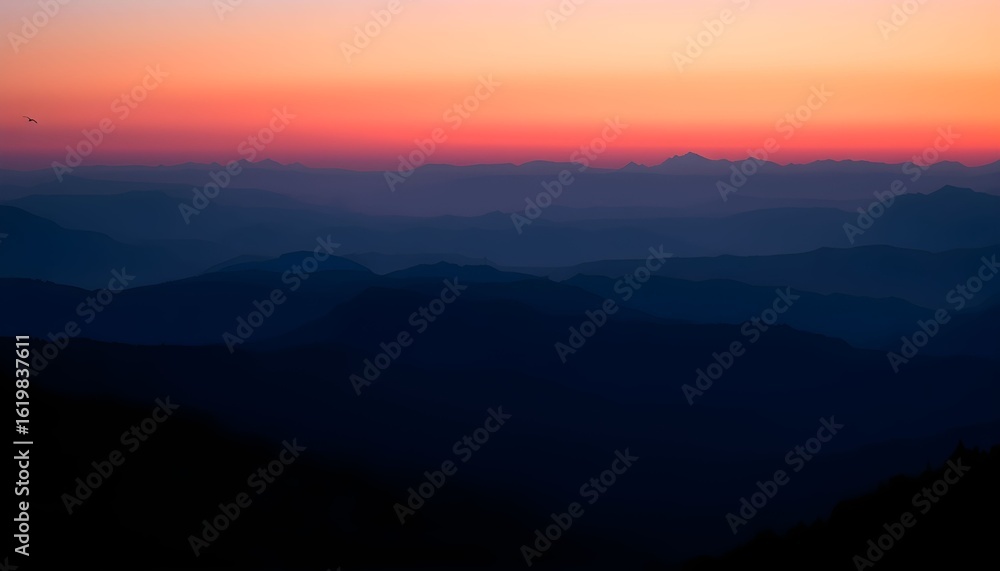 Obraz premium Layers of dark mountain silhouettes are seen against a vibrant orange and pink sunset sky.
