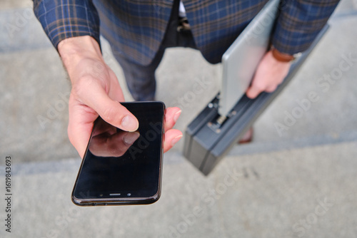 Wallpaper Mural Business professional holding smartphone and laptop briefcase outdoors during work hours in an urban setting Torontodigital.ca