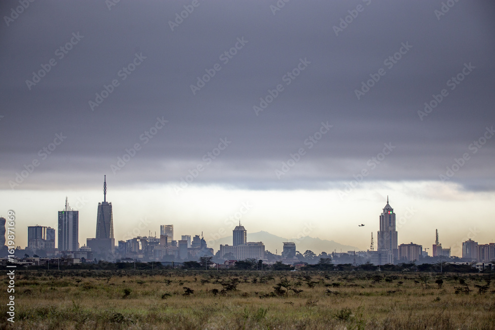 View of the Nairobi skyline emerging from the horizon, skyscrapers piercing the sky under a moody, grey cloud cover, Nairobi, Nairobi County, Kenya. View of the Nairobi skyline emerging from the horizon, skyscrapers piercing the sky under a moody, grey cloud cover, Nairobi, Nairobi County, Kenya.